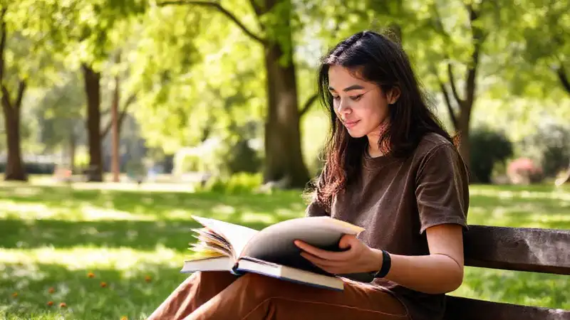 Estudiante en parque con libros y laptop